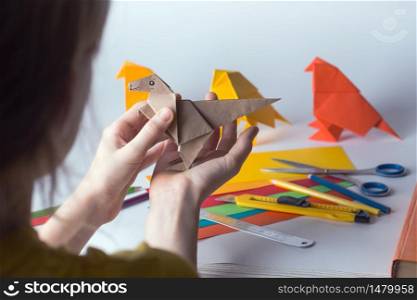 girl makes origami dinosaur of colored paper. paper, ruler, pencils, knife. interesting hobby