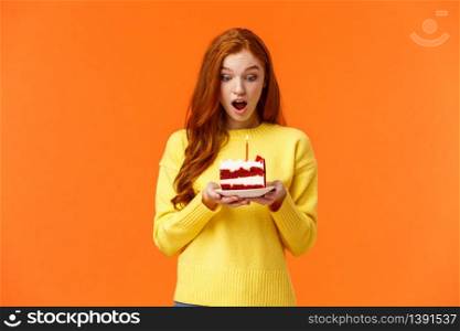 Girl making wish, receive birthday cake with one candle, celebrating b-day, receive surprise feeling amused and grateful, look at dessert with admiration and happy expression, orange background.. Girl making wish, receive birthday cake with one candle, celebrating b-day, receive surprise feeling amused and grateful, look at dessert with admiration and happy expression, orange background