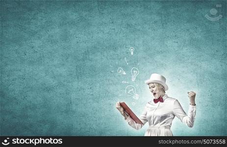 Girl mastering science. Young emotional woman in white cylinder with book in hand