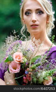 Girl model blonde in a lilac dress with a bouquet with a green forest