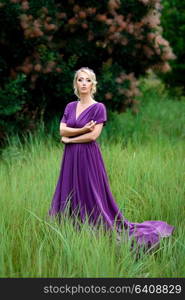 Girl model blonde in a lilac dress with a bouquet with a green forest