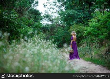 Girl model blonde in a lilac dress with a bouquet with a green forest