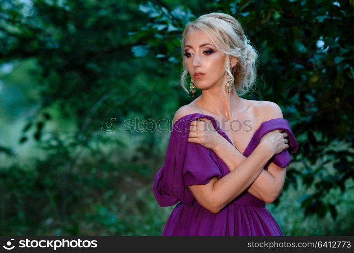 Girl model blonde in a lilac dress with a bouquet with a green forest