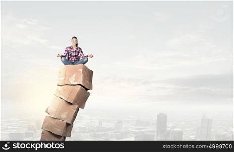 Girl on carton boxes. Smiling young woman sitting on carton boxes and meditating