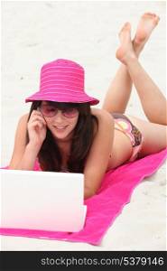 Girl on the beach with pink hat and computer
