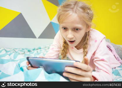 girl on the bed in the nursery play on the tablet