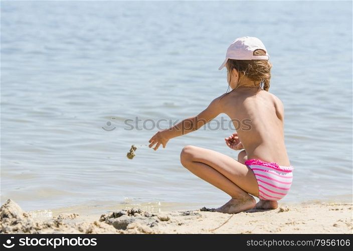 Girl on the river throws sand in water. Girl sitting on the river bank and throwing sand in the water