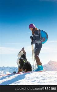 Girl on top of a mountain in winter with skiing and its Bernese dog friend