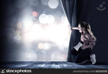 Girl opening curtain. Young woman in casual with megaphone opening curtain