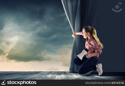 Girl opening curtain. Young woman in casual with megaphone opening curtain