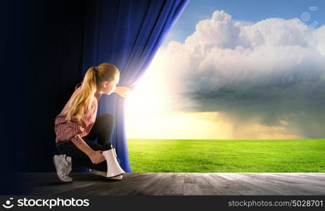 Girl opening curtain. Young woman in casual with megaphone opening curtain