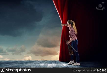 Girl opening curtain. Young woman in casual with violin opening curtain