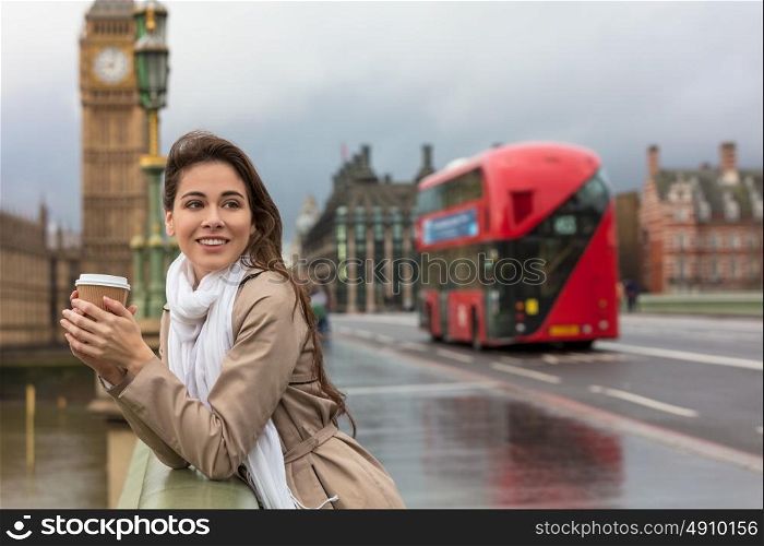 Girl or young woman drinking coffee in a disposable cup on Westminster Bridge with Big Ben and red double decker bus in the background, London, England, Great Britain