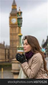 Girl or young woman drinking coffee in a disposable cup on Westminster Bridge with Big Ben in the background, London, England, Great Britain