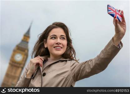 Girl or young woman tourist on vacation taking a selfie photograph by Big Ben with Union Jack cell phone, London, England, Great Britain