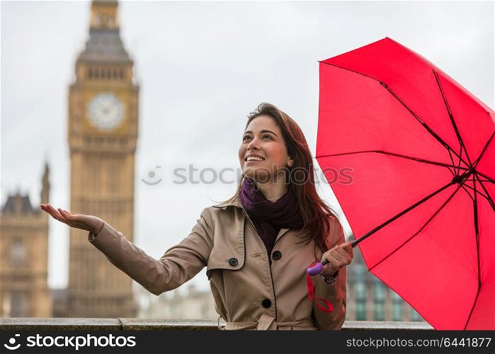 Girl or young woman with a red umbrella, hand out, checking for rain by Big Ben, London, England, Great Britain