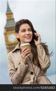 Girl or young woman with perfect teeth drinking coffee in a disposable cup and using a mobile cell phone with Big Ben in the background, London, England, Great Britain