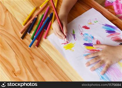 Girl painting on paper sheet with colour pencils on the wooden table at home / child kid doing drawing picture and colorful crayon