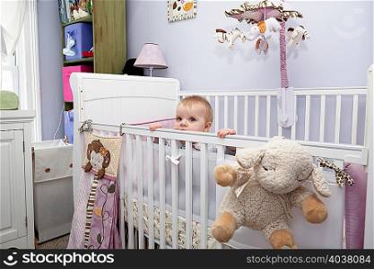Girl peering over cot railings in nursery, portrait