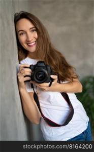 girl photographer with a camera smiling near the wall