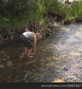 Girl picking up something in stream of water