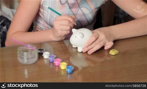 girl plans colouring borders on pig-coin box.