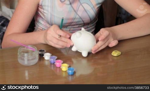 girl plans colouring borders on pig-coin box.