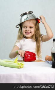 Girl playing in a cook. Carried away by the game she put on a colander on his head. Studio. Light background.