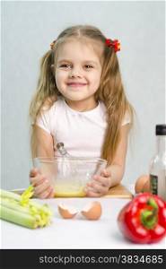 Girl playing in a cook. Girl churn whisk the eggs in a glass bowl. At the forefront of the shell, celery, pepper. Studio. Light background.