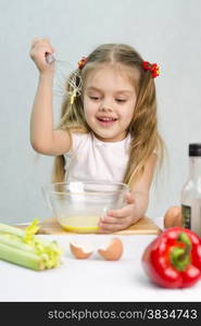 Girl playing in a cook. Girl churn whisk the eggs in a glass bowl. At the forefront of the shell, celery, pepper. Studio. Light background.