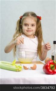 Girl playing in a cook. Girl churn whisk the eggs in a glass bowl. At the forefront of the shell, celery, pepper. Studio. Light background.