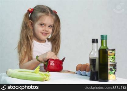 Girl playing in a cook. Girl cuts the knife red pepper. In the foreground lies celery. On the right are the bottles with the sauce, banks with green peas and corn. Studio. Light background.