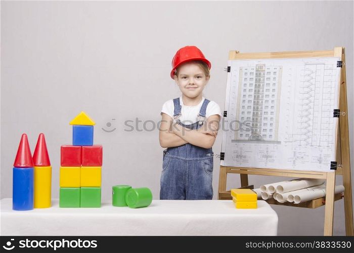 Girl playing in the Builder builds a set of cubes house. In the background on the easel fixed drawing of a house