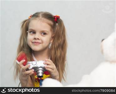 Girl playing in the photographer. Girl takes photo of Teddy digital camera and compares the result with the original.