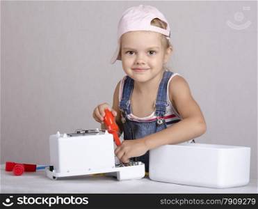 Girl playing in the repairer and repairs toy microwave. Girl Holding a screwdriver and looks in a frame
