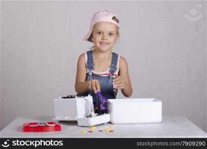 Girl playing in the repairer and repairs toy microwave. Girl Holding a pair of pliers, and looks in the frame