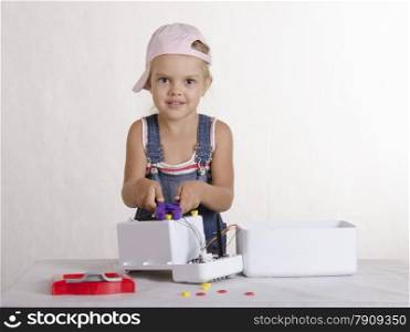 Girl playing in the repairer and repairs toy microwave. A girl Holds the pliers and twisted them nut and looks in a frame