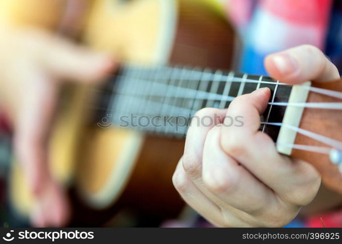 girl playing on ukulele. hands playing a guitar close-up