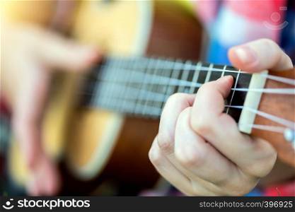 girl playing on ukulele. hands playing a guitar close-up