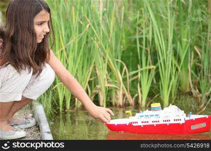 Girl playing with a toy boat on a lake