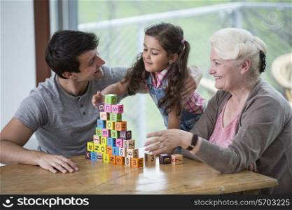 Girl playing with alphabet blocks by father and grandmother at table in house