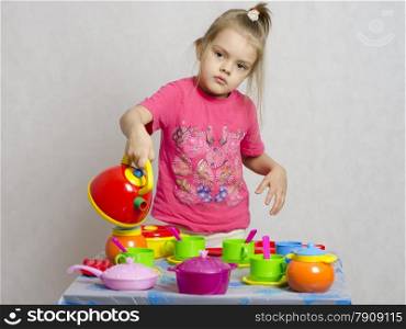 Girl plays child kitchen utensils. She picked up the teapot and poured a schematic of the water from the kettle into the Cup.