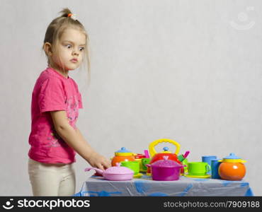 Girl plays child kitchen utensils. The girl is left of the table and looks in the frame