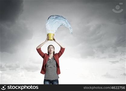 Girl pouring water from bucket. Young woman in red jacket holding yellow bucket in hands