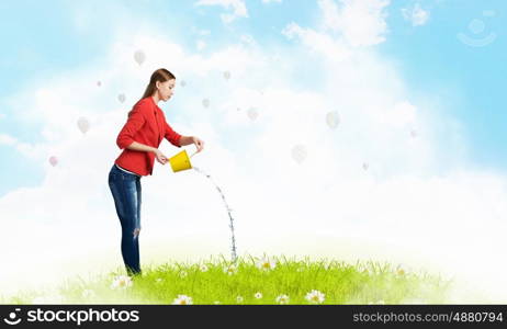 Girl pouring water from bucket. Young woman in red jacket holding yellow bucket in hands