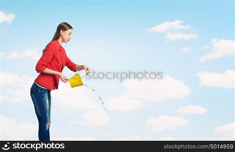 Girl pouring water from bucket. Young woman in red jacket holding yellow bucket in hands
