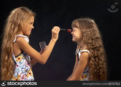 Girl powdering nose to her sister, sister squinting from tickling
