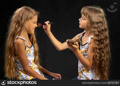 Girl powdering with a brush a nose to another girl, studio, black background