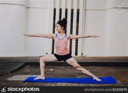 Girl practicing yoga Warrior II pose outdoors. Latin woman doing yoga warrior pose outdoors. Young woman doing yoga virabhadrasana II outdoors