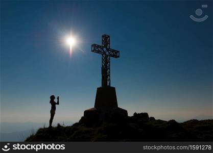 Girl prays in front of the mountain to the summit cross